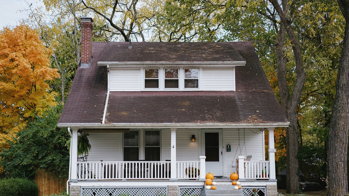 A white two-story house with a front porch, surrounded by autumn trees.